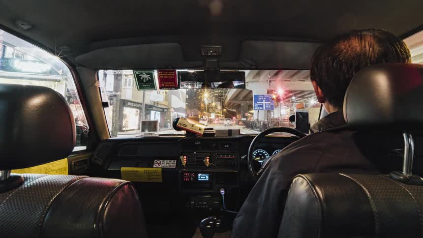 View from the back seat of an automobile as a man drives through busy downtown traffic at night and the city lights shine