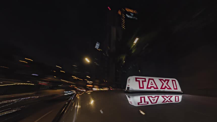 Time lapse of taxi moving through city streets next to illuminated buildings at night