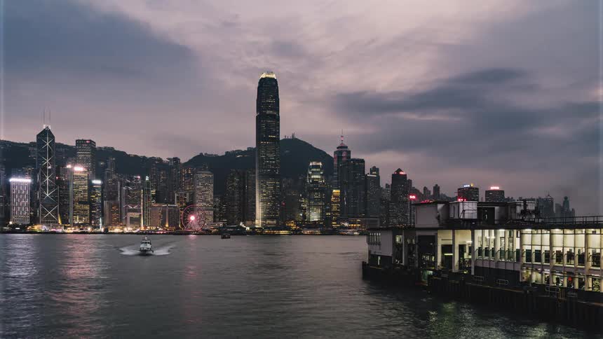 Water vessels move across harbor as night falls