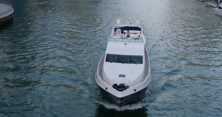 Three people ride on top of boat moving through water near marina