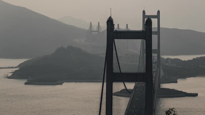 Water vessels pass underneath busy suspension bridge on foggy day
