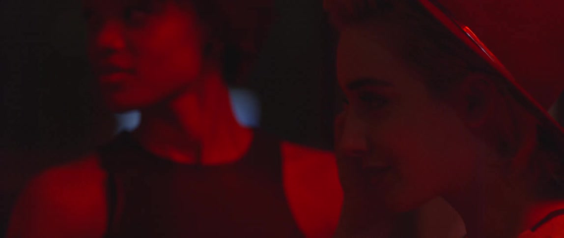 Two women interact in a dimly lit space filled with red light