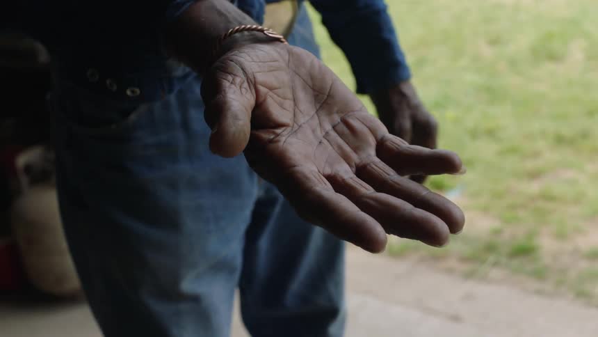 An old man is standing in a doorway with his hand out