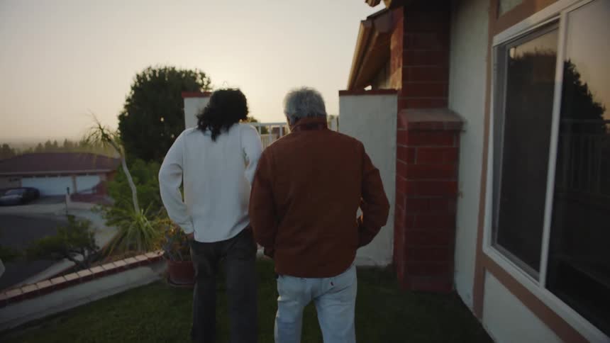 A father and son walk toward their house and enter through a gate