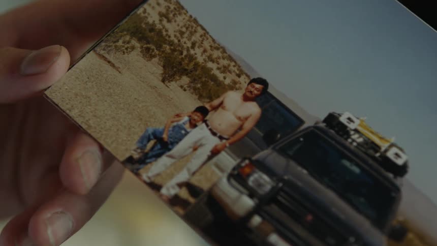 A person is holding an old photo of a father and son
