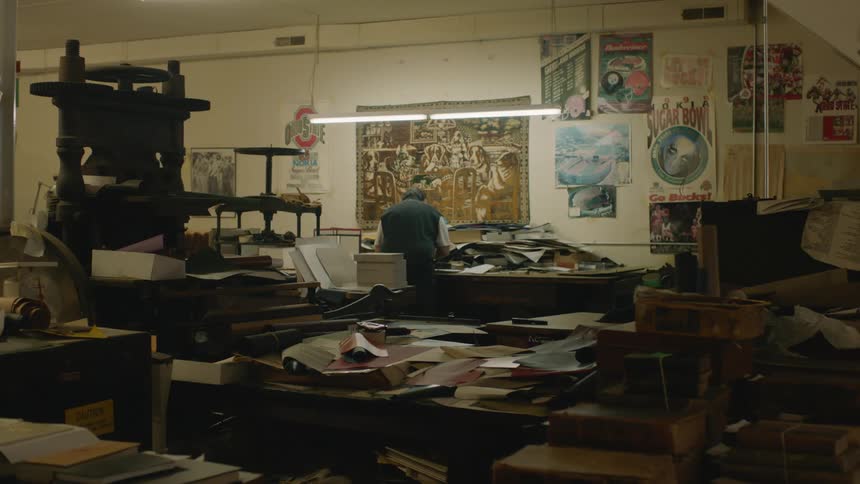 Man works in print shop littered with papers and old printing presses