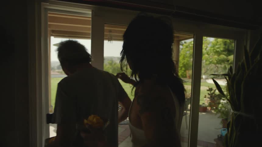 Two men carry food as they go through a sliding glass door outside to a porch