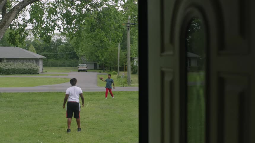 Two boys playing catch with a football in the front yard of their neighborhood home