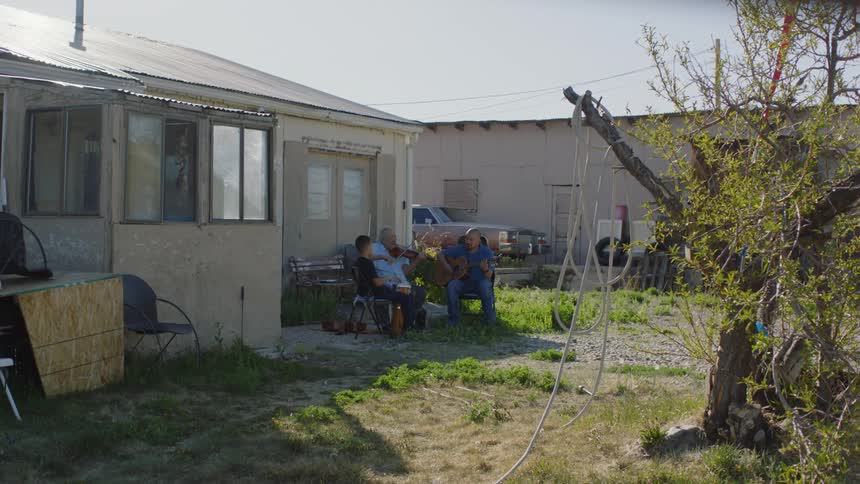 A family sits in their backyard playing guitar and singing togethe