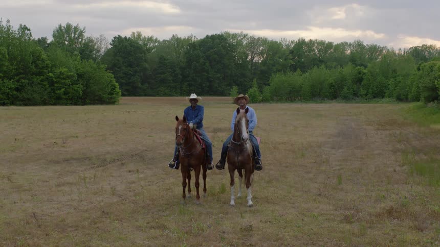 Two men sitting on horses stopped in the grass side by side
