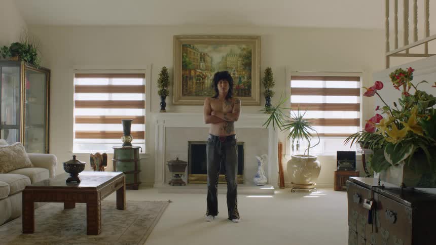 You shirtless asian man with tattoos stands posing in middle of living room