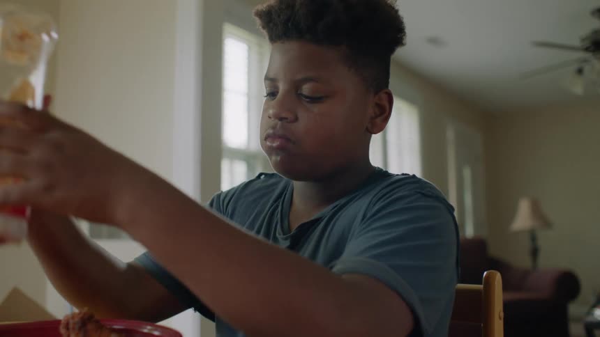 A boy shakes and squeezes the ketchup bottle to get some on his dinner plate