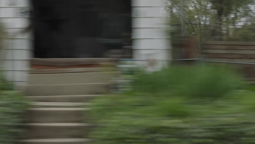 A vehicle drives through a small town neighborhood with older homes