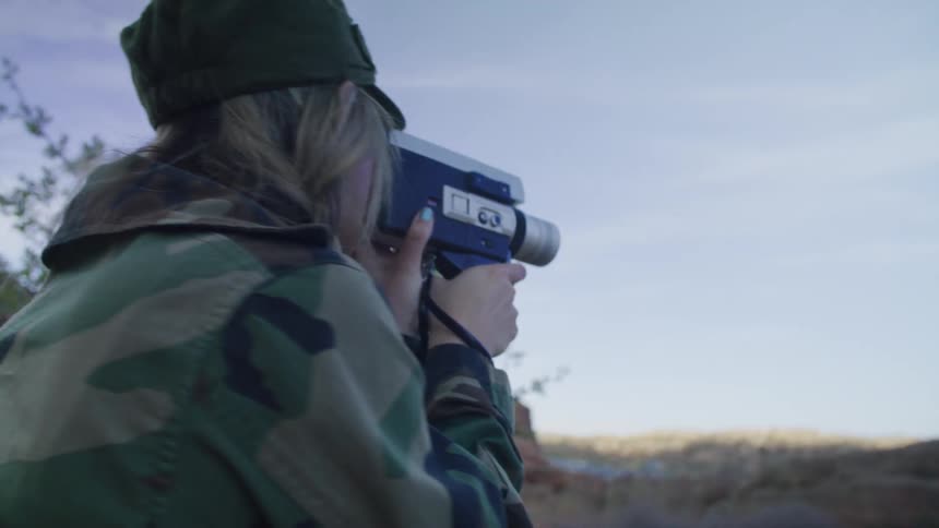 A woman is using a camcorder to film the mountains around her