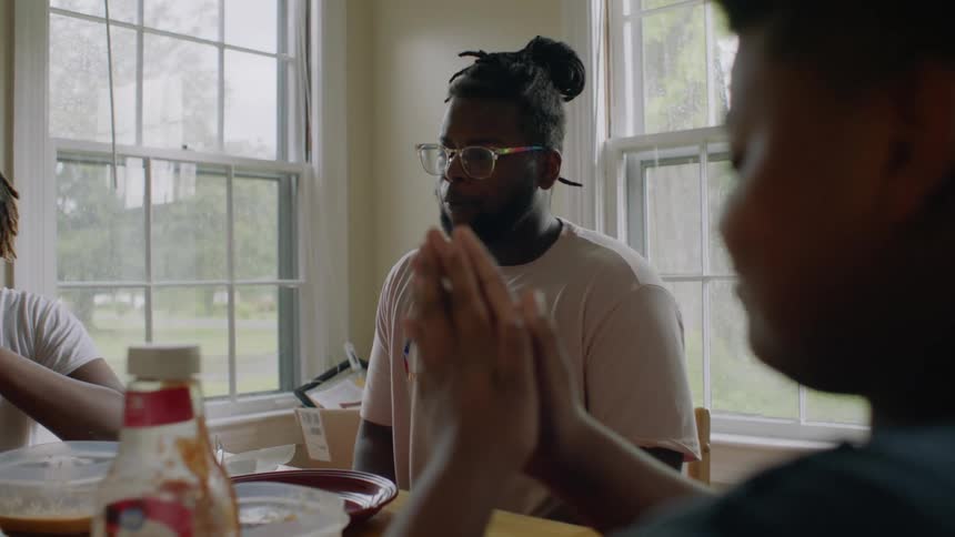 A man sitting at a dining table says grace as a pair of teenagers pray along with him