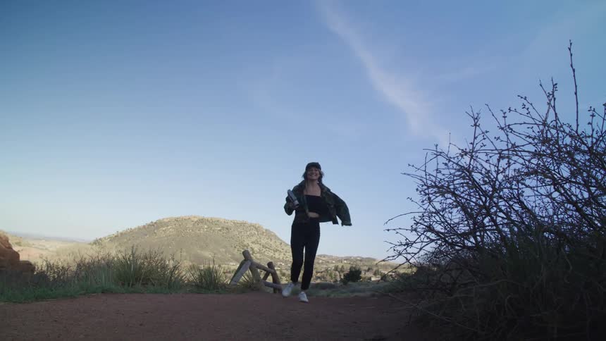 A teenage girl carrying a book is running on a path and there is a mountain in the distance