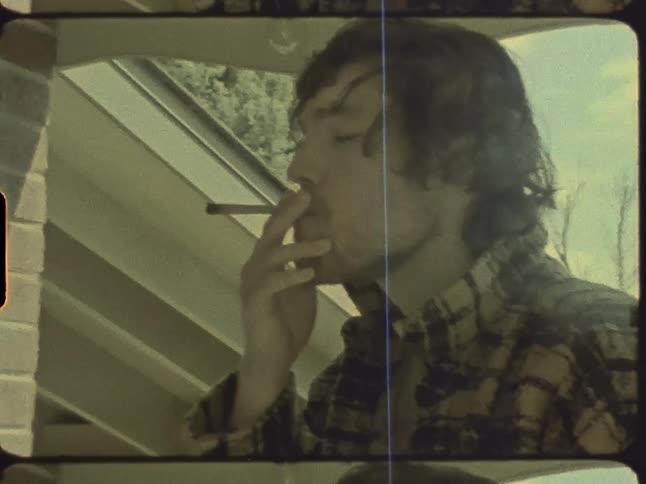 A man is outside next to a house smoking a cigarette