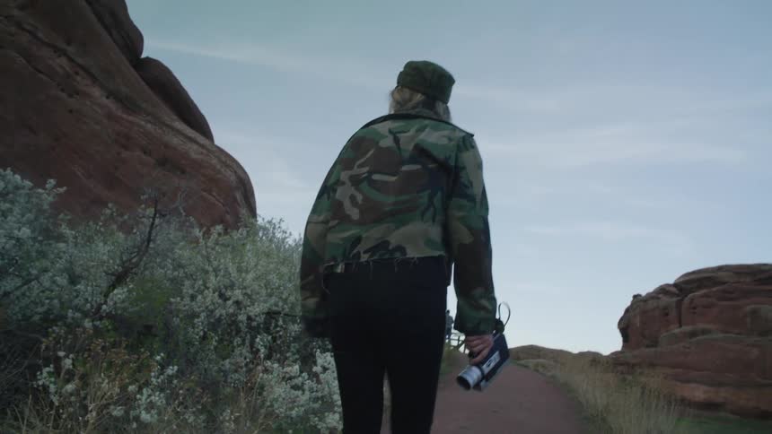 A woman carries a camcorder while hiking through a canyon