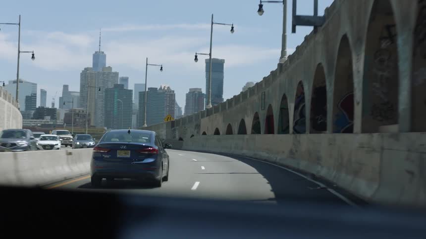 Cars driving down a street with the New York City city skyline in the distance