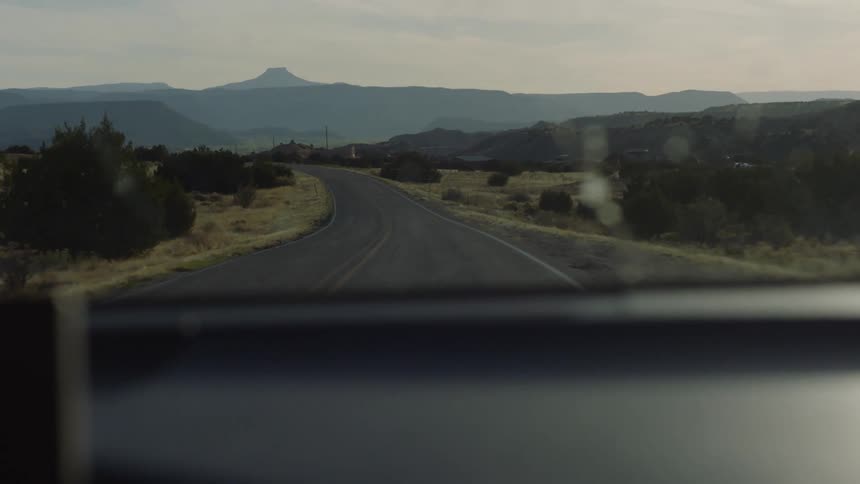A car traveling on an empty road toward the cerro pedernal on the horizon