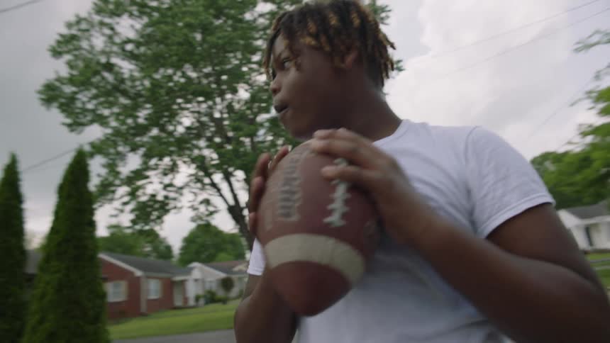 A teenage boy throws a football in a neighborhood