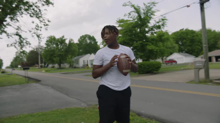 A teenage boy is in a neighborhood field as he catches a football and passes it to another boy