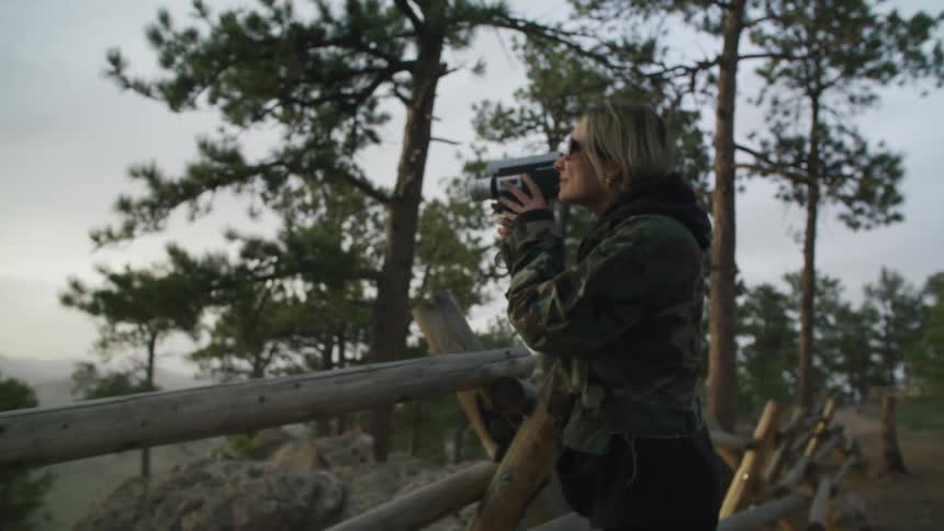 A woman pauses at an overlook on the trail leans on the fence to film