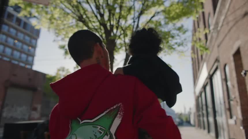 Man carries son along sidewalk near building on sunny day