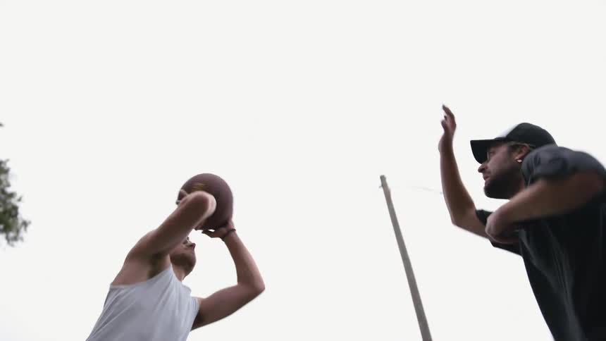 A man is dribbling a basketball and another man tries to block him as he takes a shot