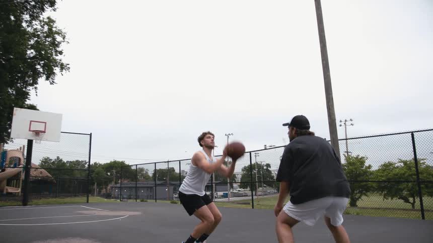 One man takes a shot as he and another man play one on one basketball in park