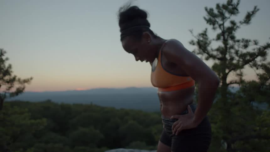 A woman takes a breather on top of a mountain at dusk
