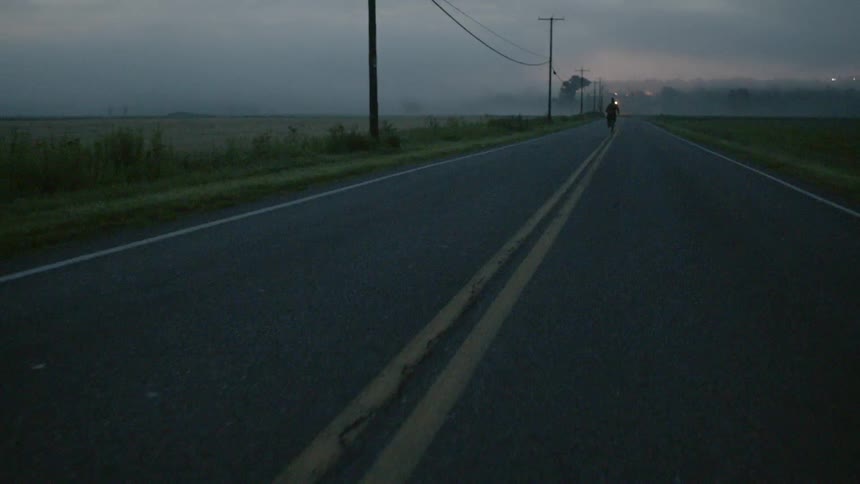 A man running down the center of a road at dusk
