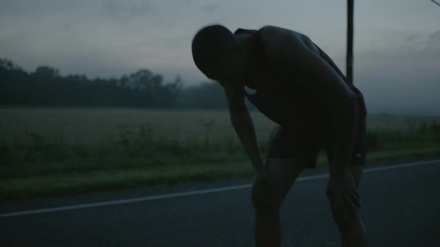A man bends over and pants on a rural road
