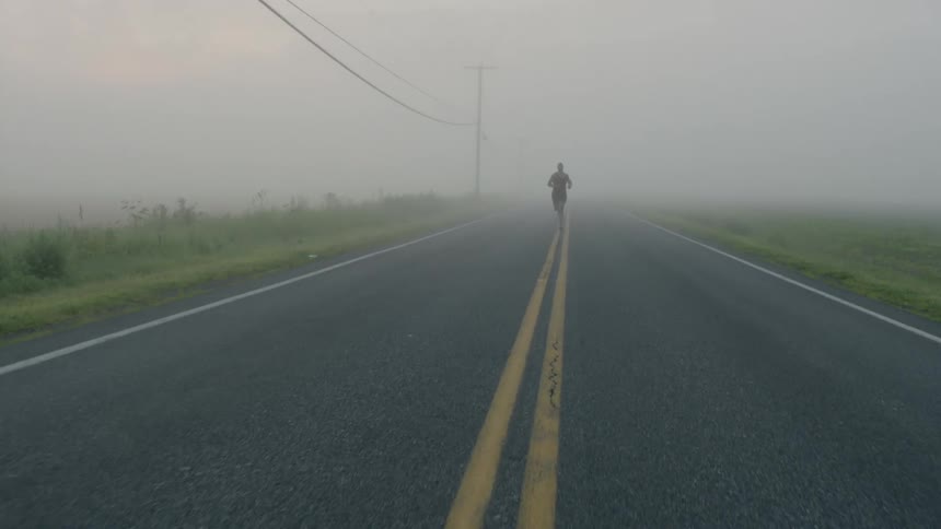 A person is running down the centerline of a road in the mist