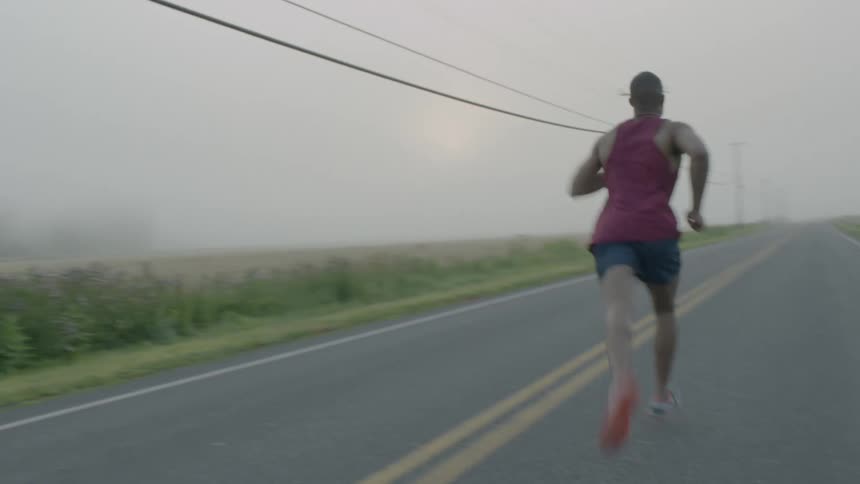 A black man looks down a road with intense concentration then begins to jog