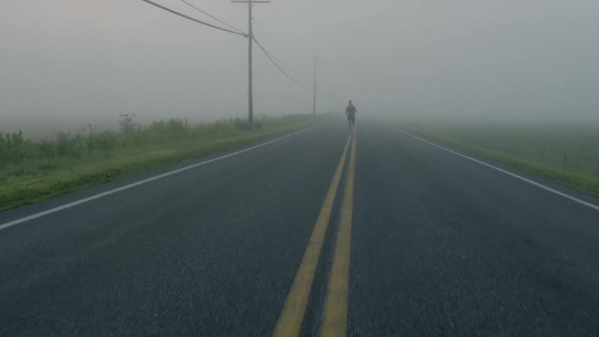 Man running down the center of a foggy road