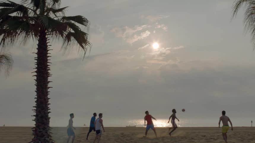 A group of men playing soccer on a beach on a cloudy day