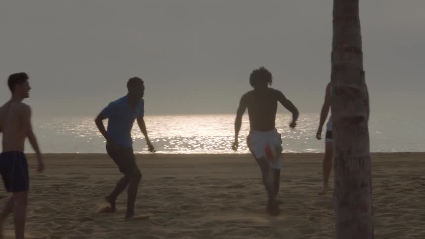 Young men playing soccer on a beach