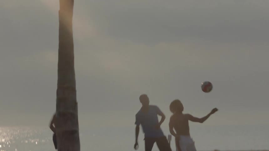 A group of men kicking a ball together on the beach