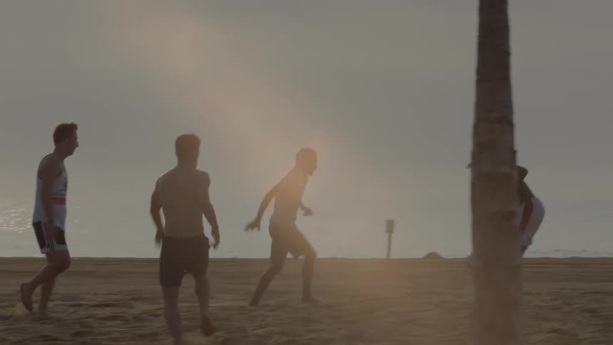 A group of guys are playing soccer on the beach
