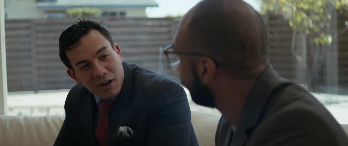 Two men are sitting down talking and one man nods his head as he listens to the other man speak