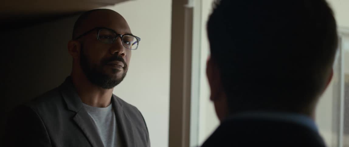 Two men are talking and one man smiles and looks around the room