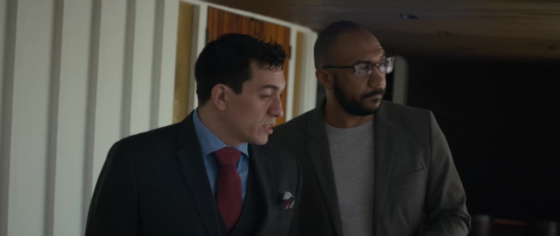 Two men are walking and talking and one man nods his head as he listens to the other man speak