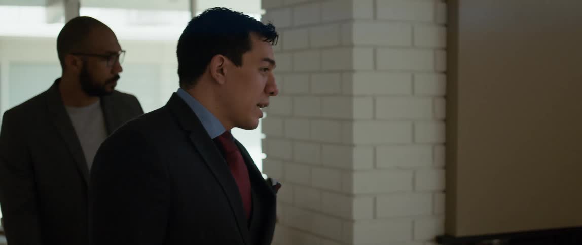 Business men walk past brick wall talking with one carrying a file folder