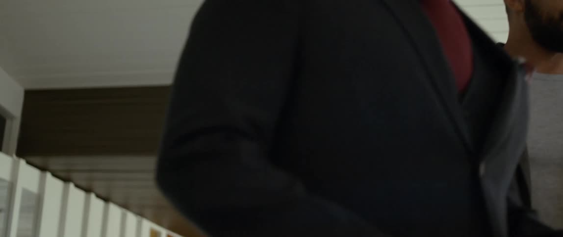 Two men are walking through a room as they talk and one man is carrying a paper