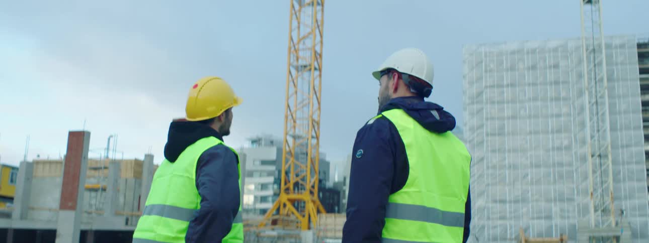 Two male construction workers wearing safety helmet and vests standing and talking at a construction site
