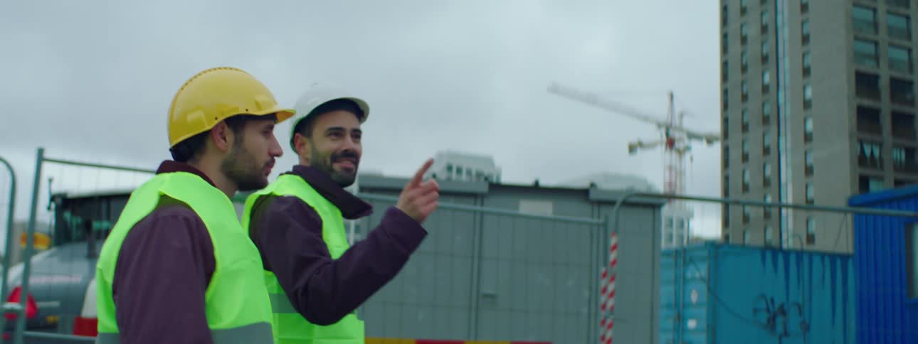 Two construction workers are walking through a construction site as the have a conversation