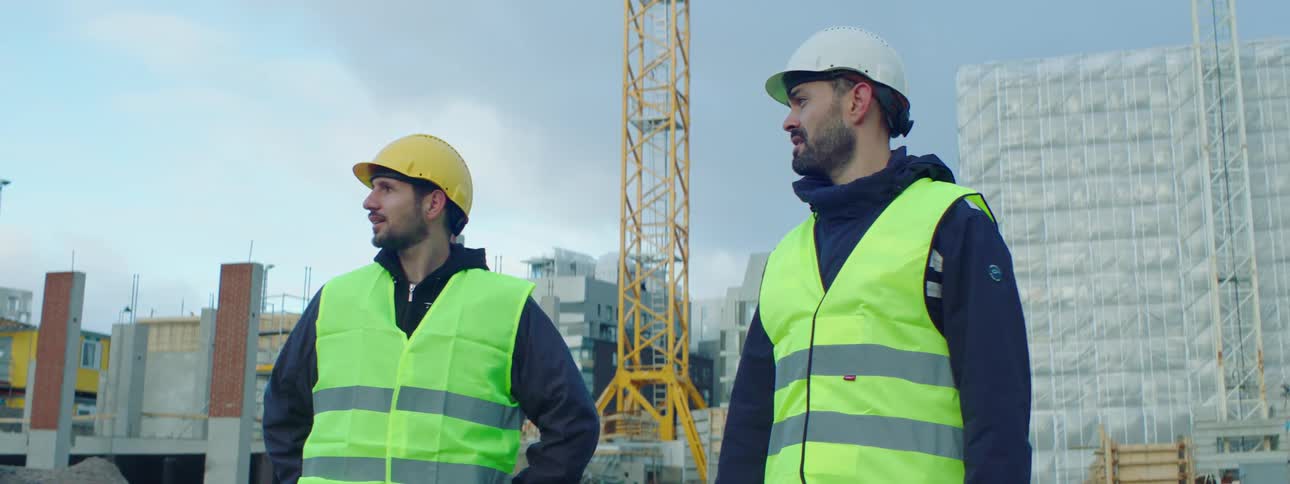 Two construction workers stand on a construction site and talk and point