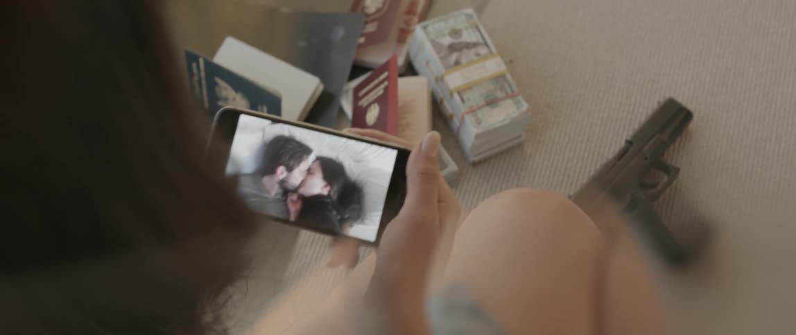 A woman holds a cellphone that is playing a video of two people kissing