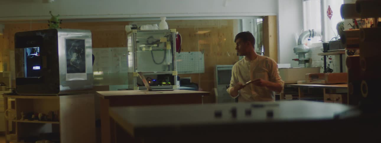 Man examines object while standing in front of laptop in maker lab